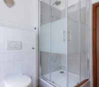 Moderní koupelna se sprchovým koutem s průhledným a matným sklem. Nástěnná toaleta a bílé dlaždice vytvářejí čistý, minimalistický vzhled.