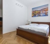 Ložnice má dvě vysoká okna s dekorativními mřížkami a červenými závěsy. Dřevěná postel je centrálně umístěna a přirozené světlo zvyšuje jas místnosti. Noční stolky jsou jednoduché a doplňují celkový klasický vzhled.
