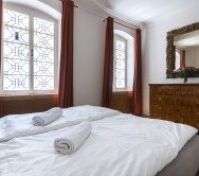 ožnice je vybavena pohodlnou postelí s bílým ložním prádlem a ručníky. Velké okna s historickými mřížemi a červenými závěsy zajišťují dostatek světla. Rustikální komoda s ozdobným zrcadlem přidává na kouzlu místnosti.